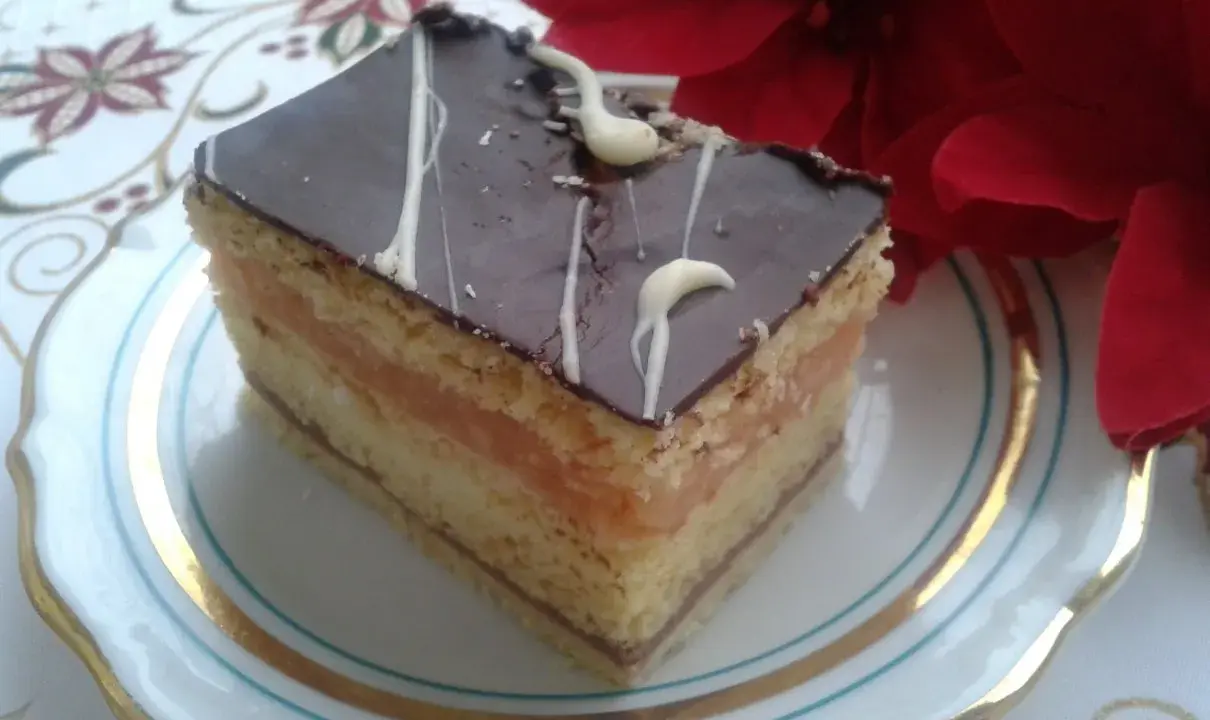Pyszny kawałek ciasta z warstwami biszkoptu, kremu serowego i jabłek, oblany czekoladą. Idealny na przepis na ciasto delicja z serem i jabłkami.