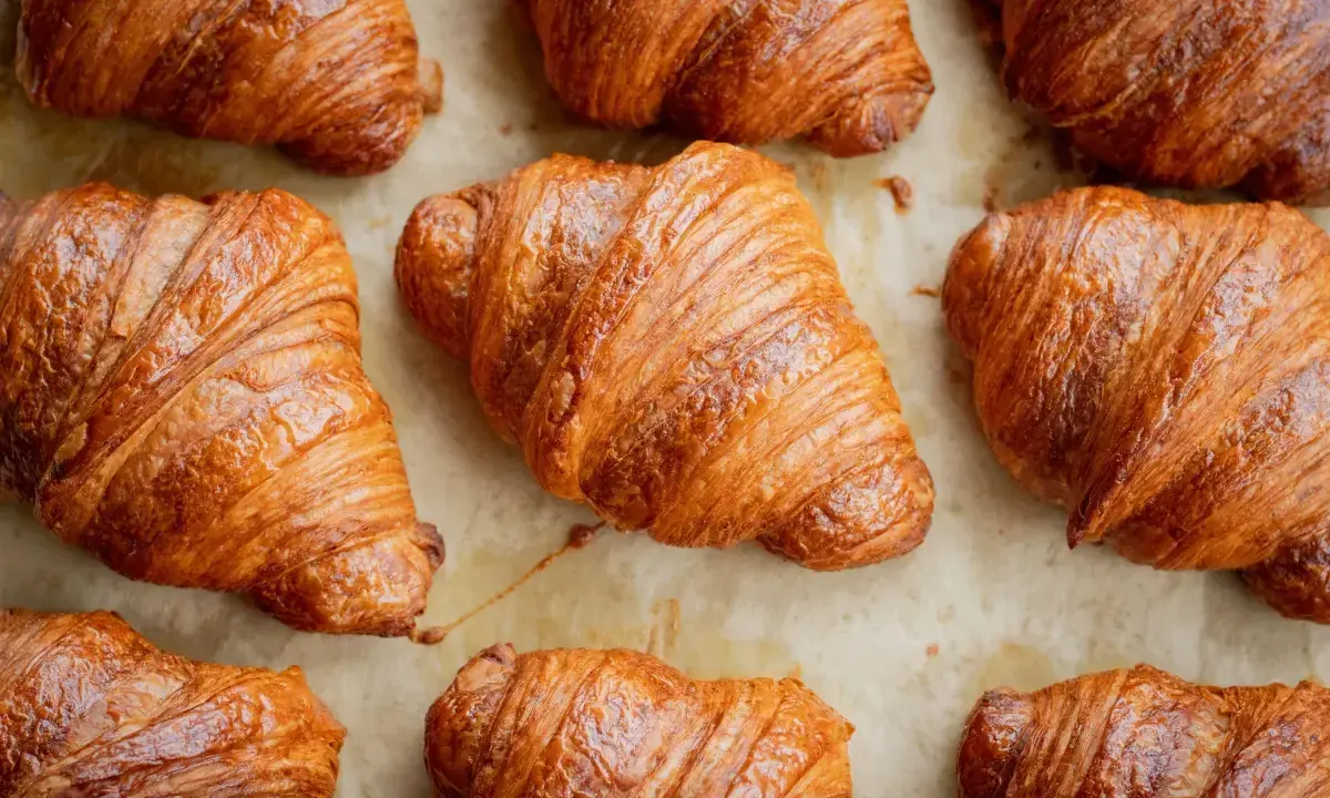 Złociste, chrupiące rogaliki ułożone na papierze do pieczenia. Idealne na śniadanie, choć warto pamiętać o ich kaloryczności – croissant kcal.