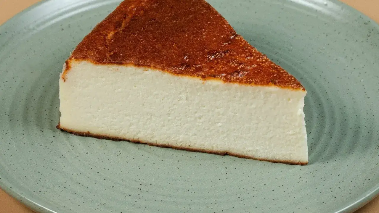 Pyszny kawałek sernika pieczonego bez spodu, z lekko przypieczoną górą, na zielonym talerzu.