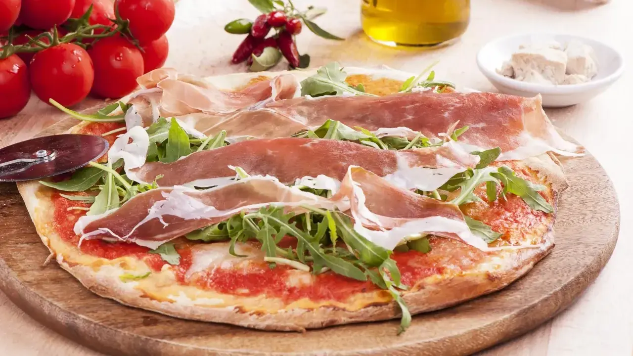 Pyszna pizza prosciutto z rukolą, pomidorkami i oliwą. Idealna na włoską ucztę.