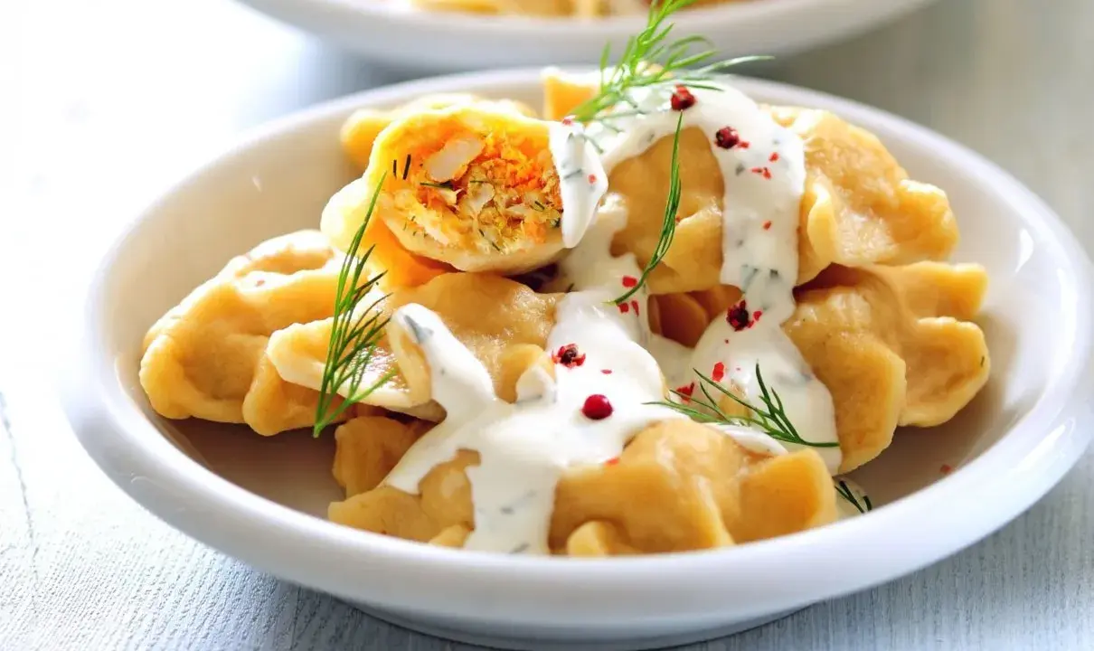 Pyszne pierogi z farszem, polane sosem i posypane koperkiem. Idealne danie, by zastanowić się, co ugotować w piątek na obiad.