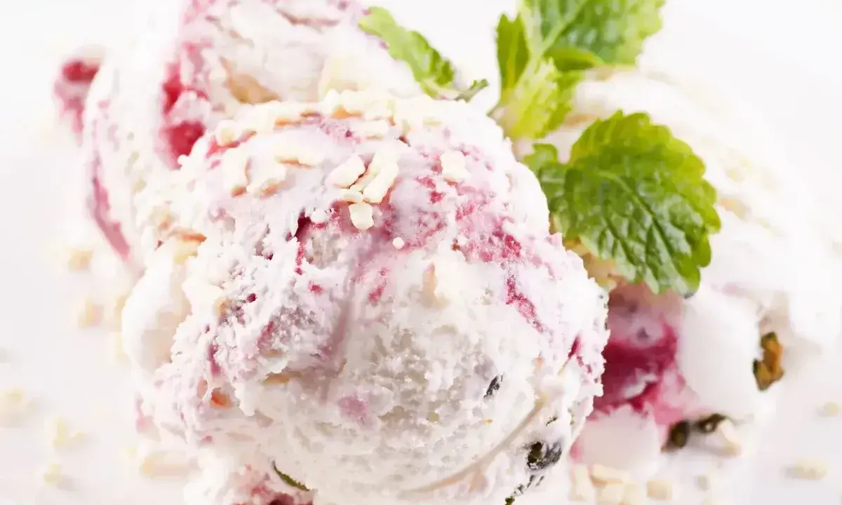 Pyszne lody z mascarpone z malinową nutą i chrupiącymi kawałkami białej czekolady, ozdobione listkiem mięty.