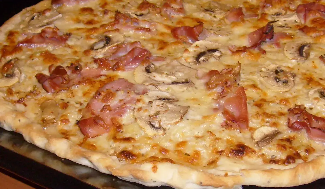 Pyszna pizza carbonara z chrupiącym boczkiem, pieczarkami i ciągnącym się serem. Idealna na szybki obiad.