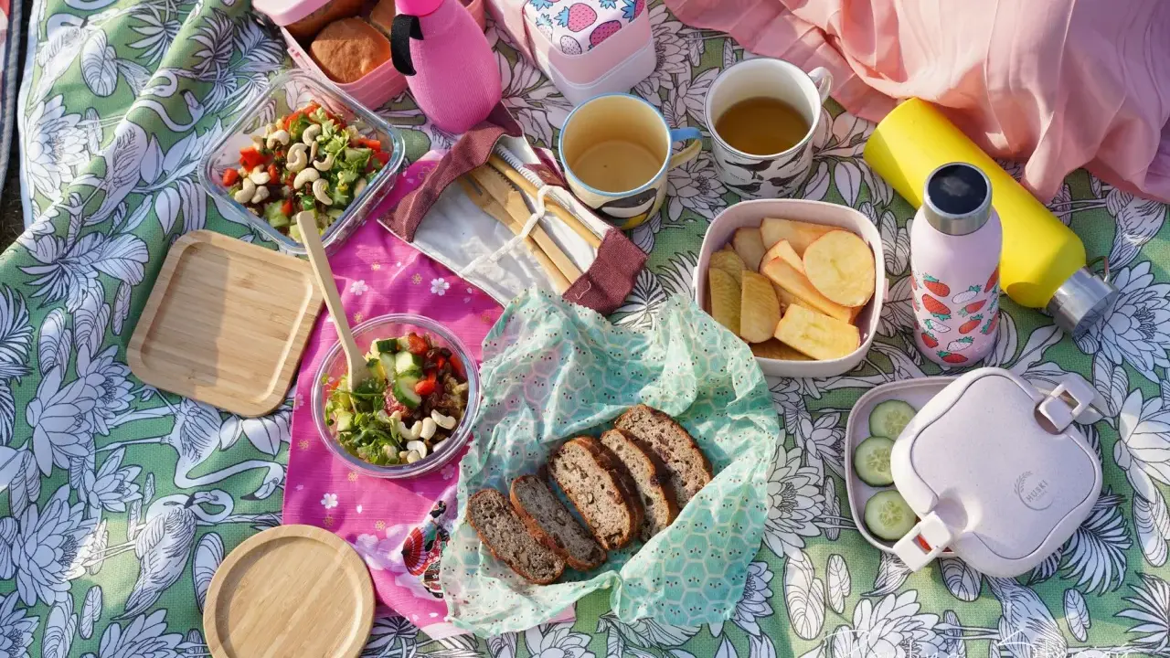 Piknikowy koc z jedzeniem: sałatki, chleb, owoce, napoje i bambuowe sztućce.