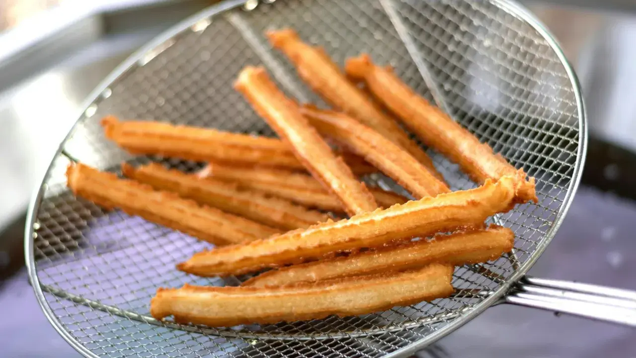 Churros co to? Złociste, chrupiące paluszki smażone na głębokim tłuszczu, wyjęte właśnie z frytownicy na metalowej łyżce cedzakowej.