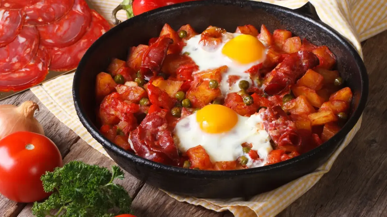 Pyszne danie z jajek na obiad: ziemniaki, chorizo, papryka i groszek zapiekane w patelni.