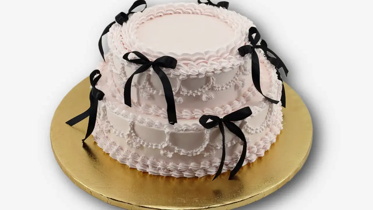 Dwupiętrowy tort w kolorze pudrowego różu, ozdobiony czarnymi wstążkami. Idealny na osiemnastkę, zastanawiasz się, ile kosztuje catering na 18?