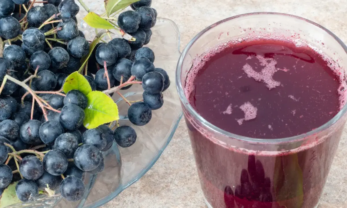 Świeża aronia na talerzu i szklanka soku. Idealne do przygotowania przetworów, np. jak mrozić aronię na zimę.
