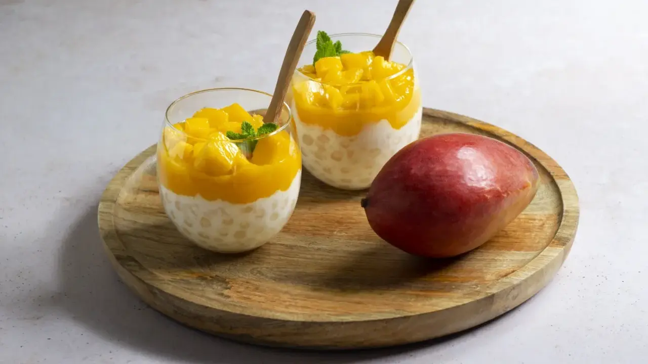 Pyszny deser z tapioki i mango, idealny sposób, by wykorzystać mrożone mango. Podany w szklankach z drewnianymi łyżeczkami.