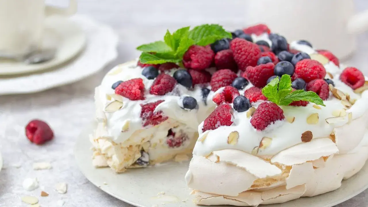 Beza Pavlova która zawsze wychodzi, udekorowana bitą śmietaną, malinami, borówkami i listkami mięty. Idealna na deser.