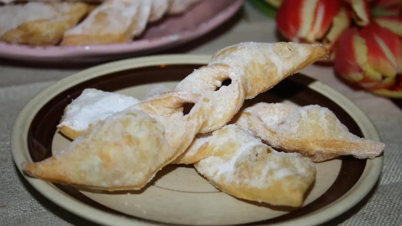 Chrupiące faworki, przepis babci, posypane cukrem pudrem, na talerzu obok tulipanów.