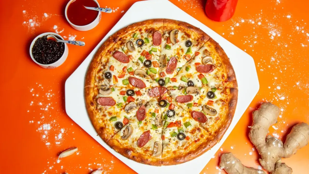 Chrupiąca pizza z pieczarkami, salami i papryką na pomarańczowym tle.