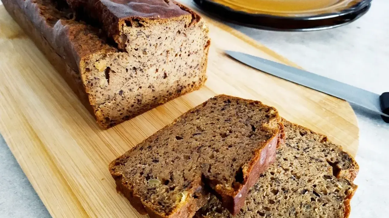 Wilgotny chleb bananowy pokrojony na desce, obok nóż i talerz.