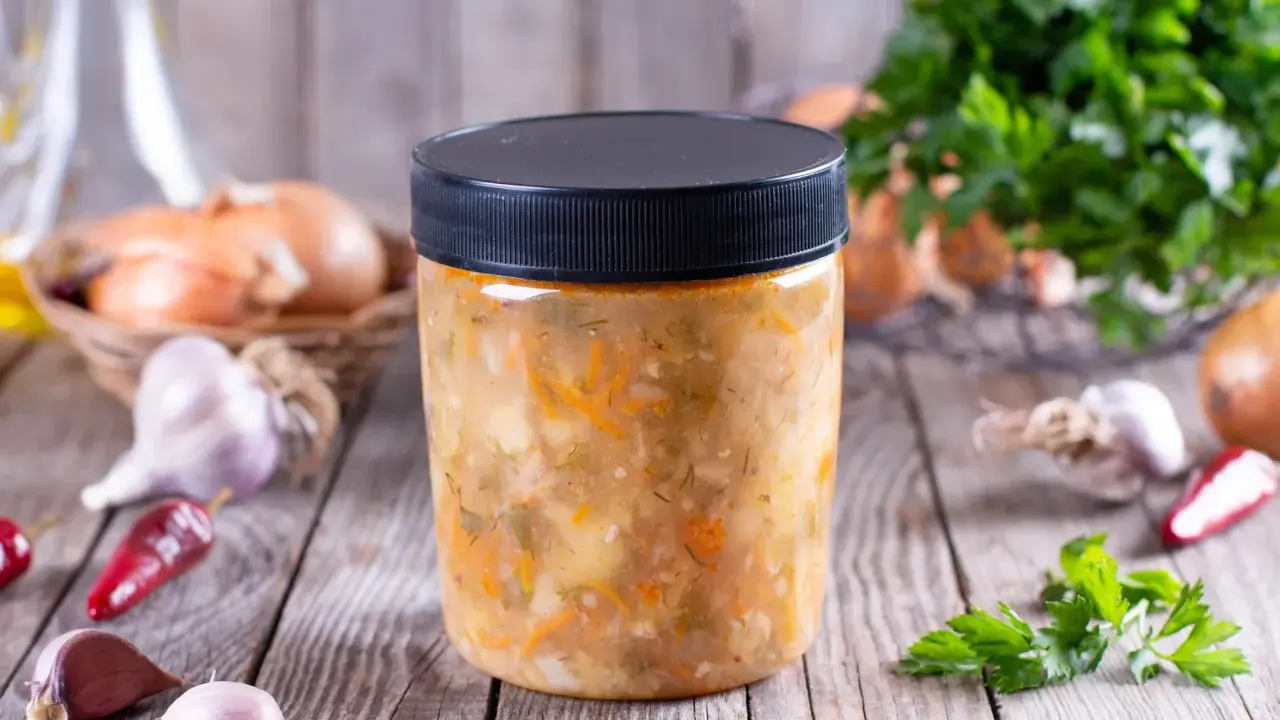 Słoik z domową zupą warzywną, obok cebula, czosnek i chili. Dowiedz się, jakich zup nie można mrozić.