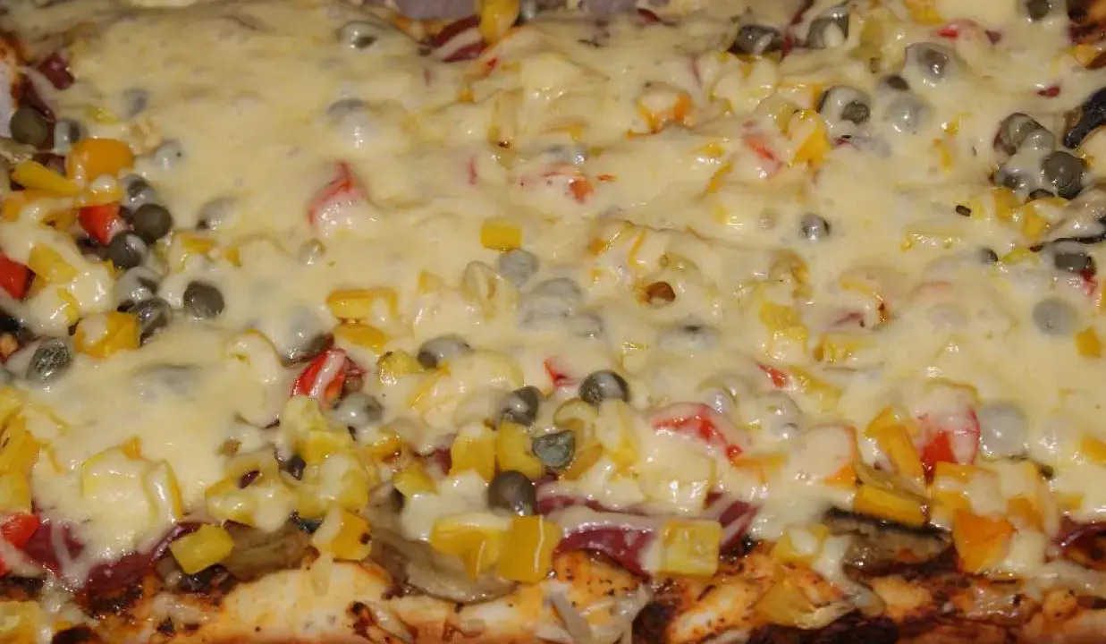 Pyszna pizza na grubym cieście z warzywami i roztopionym serem.