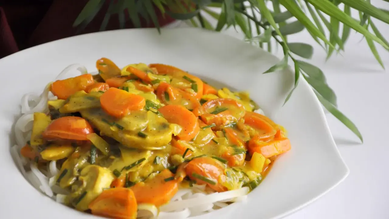 Zdrowy obiad: makaron ryżowy z warzywami w sosie curry. Kolorowe marchewki i inne warzywa tworzą apetyczną kompozycję.
