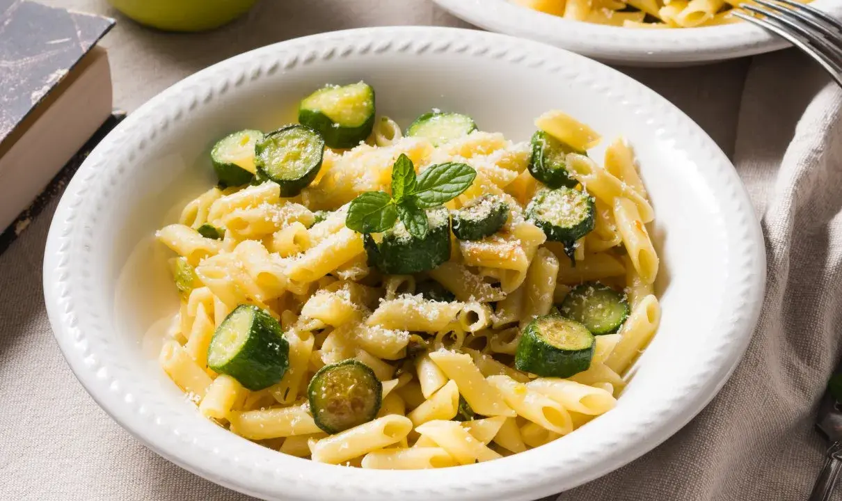 Pyszne danie z makaronem penne i kawałkami cukinii, posypane parmezanem i listkami mięty. Idealne co z cukinii na obiad!