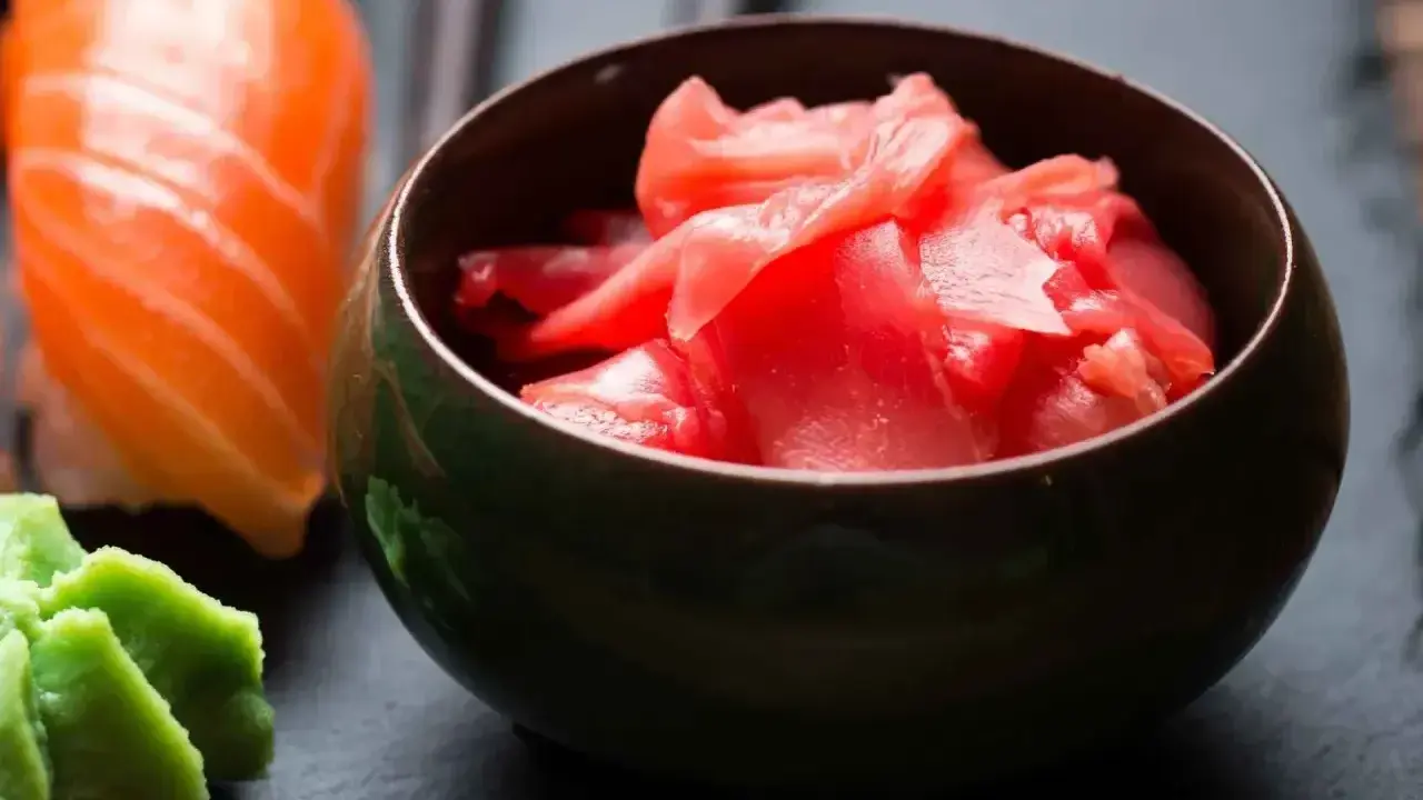 Miseczka z marynowanym imbirem do sushi, obok kawałka sushi z łososiem i wasabi.