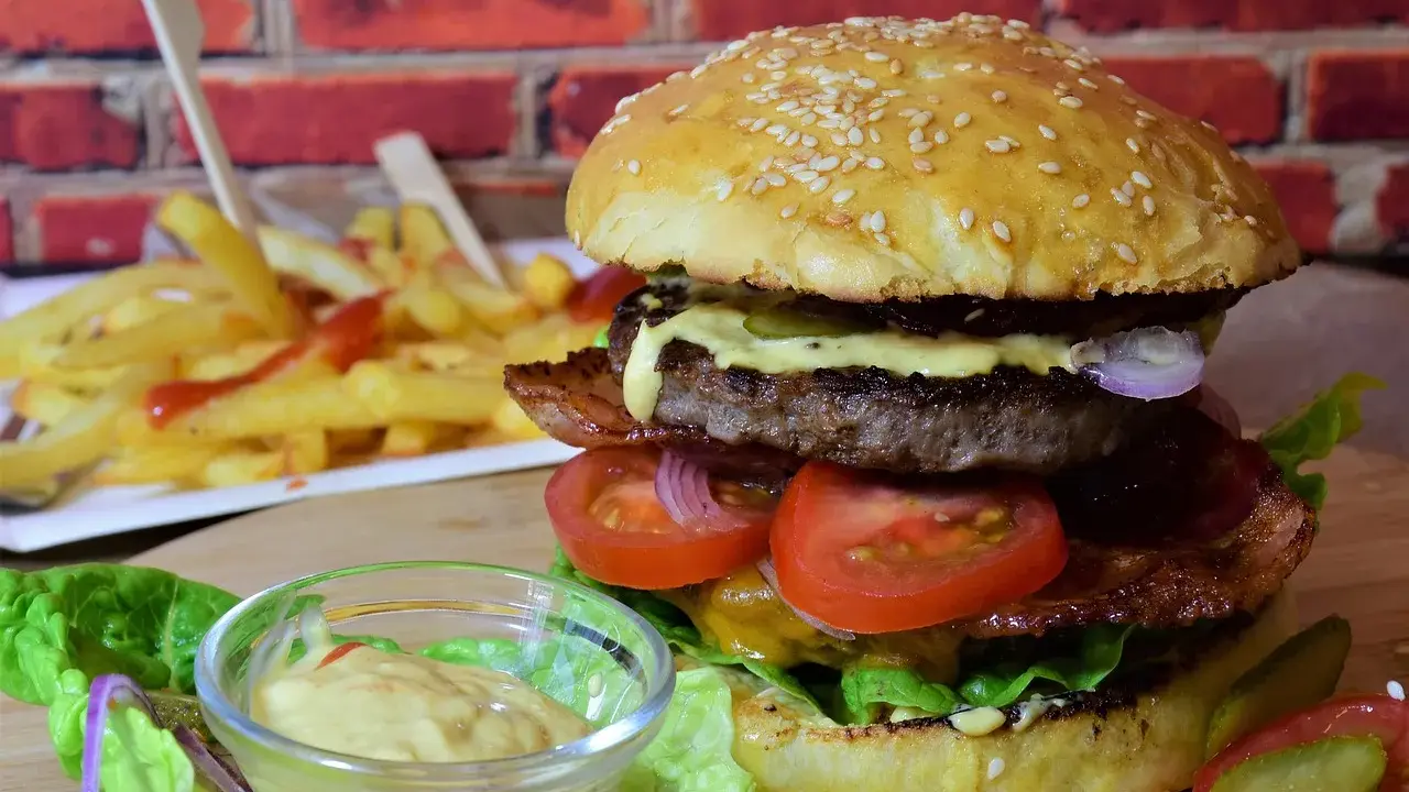 Soczysty burger z wołowiny, bekonem, warzywami i frytkami w tle.