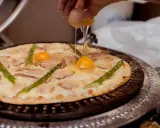 Pizza z jajkiem i szparagami, na którą wylewane jest surowe jajko.
