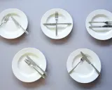 Pięć talerzy z różnie ułożonymi sztućcami, wskazujących jak jesc catering.