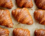 Złociste, chrupiące rogaliki ułożone na papierze do pieczenia. Idealne na śniadanie, choć warto pamiętać o ich kaloryczności – croissant kcal.