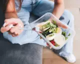 Kobieta z widelcem w dłoni je sałatkę z kurczakiem i jajkiem z pudełka. Zastanawiasz się, jaki catering dietetyczny wybrać?