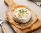 Pyszny camembert z grilla, zapieczony z ziołami, na drewnianej desce. Idealny do maczania.