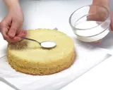 Ręka z łyżeczką nasącza biszkopt, obok szklana miseczka z płynem.