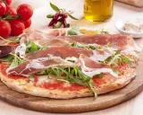 Pyszna pizza prosciutto z rukolą, pomidorkami i oliwą. Idealna na włoską ucztę.