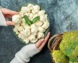 Ręce trzymające różyczki kalafiora nad talerzem, obok koszyk z brokułami. Zastanawiasz się, czy można mrozić kalafior? Tak, można!