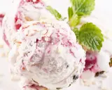 Pyszne lody z mascarpone z malinową nutą i chrupiącymi kawałkami białej czekolady, ozdobione listkiem mięty.