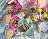 Piknikowy koc z jedzeniem: sałatki, chleb, owoce, napoje i bambuowe sztućce.