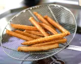 Churros co to? Złociste, chrupiące paluszki smażone na głębokim tłuszczu, wyjęte właśnie z frytownicy na metalowej łyżce cedzakowej.