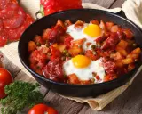 Pyszne danie z jajek na obiad: ziemniaki, chorizo, papryka i groszek zapiekane w patelni.
