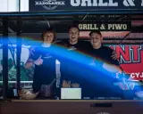 Trzech uśmiechniętych mężczyzn za ladą cateringową z napisem "Grill & Piwo".
