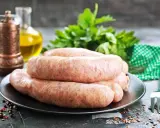 Świeża kiełbasa na talerzu, obok przyprawy i ziół. Zastanawiasz się, jak długo można mrozić kiełbasę?