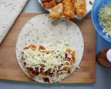 Tortilla z kurczakiem, serem i sosem na desce. Obok miska z serem i butelka ketchupu.