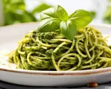 Porcja spaghetti z zielonym pesto, udekorowana listkami bazylii.