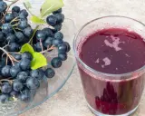 Świeża aronia na talerzu i szklanka soku. Idealne do przygotowania przetworów, np. jak mrozić aronię na zimę.