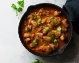 Serca drobiowe w gęstym, aromatycznym sosie, udekorowane świeżą natką pietruszki, podane w żeliwnej patelni.