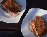 Dwa kawałki tiramisu posypane kakao na białych talerzach. Idealne do mocnej kawy, która podkreśli smak.
