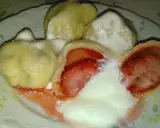 Jak gotować pierogi mrożone z truskawkami? Na talerzu pyszne, gorące pierogi z owocami, polane śmietaną i cukrem.