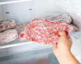 Ręka wyjmuje z zamrażarki worek z mrożonym mięsem. To idealny sposób, w czym mrozić mięso, by zachować jego świeżość.