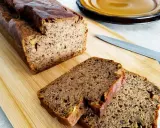 Wilgotny chleb bananowy pokrojony na desce, obok nóż i talerz.