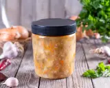 Słoik z domową zupą warzywną, obok cebula, czosnek i chili. Dowiedz się, jakich zup nie można mrozić.
