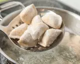 Mrożone pierogi na łyżce cedzakowej nad gotującą się wodą.