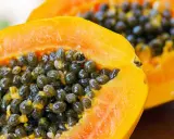 Dwa soczyste kawałki papaya z mnóstwem czarnych nasion w środku.