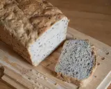 Chleb z siemienia lnianego, z jedną kromką obok, na desce do krojenia.
