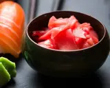 Miseczka z marynowanym imbirem do sushi, obok kawałka sushi z łososiem i wasabi.